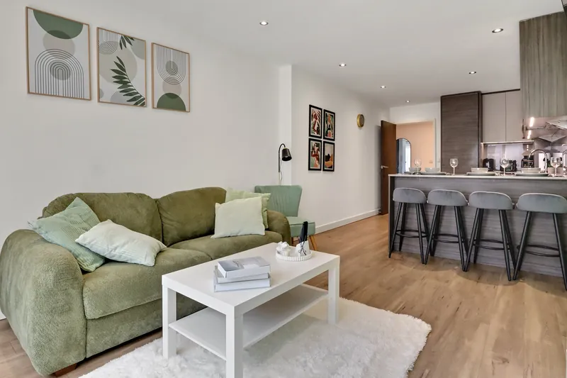 Open-plan living room with green sofa and kitchen bar